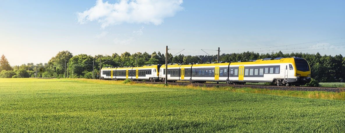 Gelbe Regionalbahn fährt an Wiese entlang