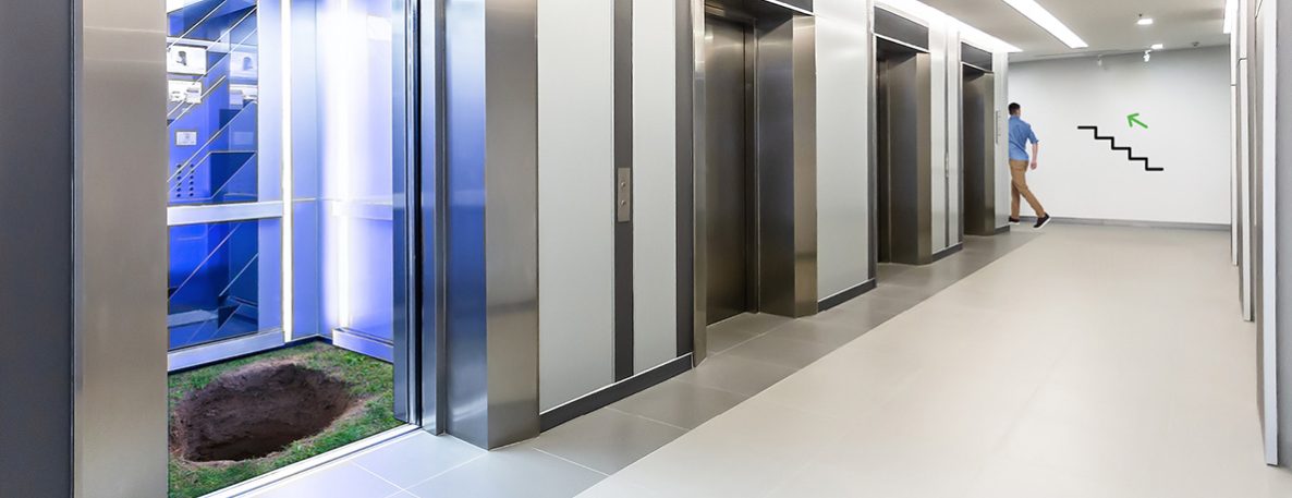 Eine geöffnete Fahrstuhltür gibt den Blick auf einen Abgrund frei. Im Hintergrund fordert ein Symbol dazu auf, lieber die Treppe zu benutzen.